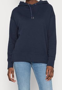 Marinblå huvtröja med avslappnad passform, med dragsko, ribbade ärmslut och rundad nederkant. Slät bomullstyg.