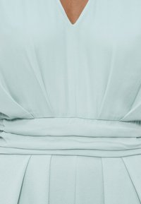 Φόρεμα σε απαλό γαλάζιο με V-λαιμόκοψη, με ραμμένο ύφασμα στη μέση και διακριτικές κάθετες πτυχώσεις στη φούστα.