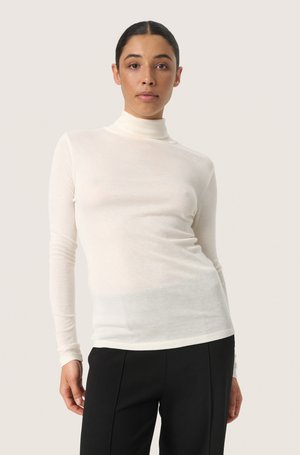 Long-sleeve turtleneck shirt in cream, made of lightweight fabric. Features a fitted design and smooth texture, paired with black trousers.