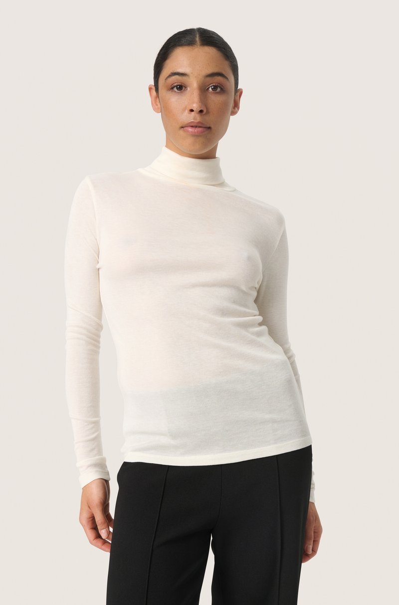 Long-sleeve turtleneck shirt in cream, made of lightweight fabric. Features a fitted design and smooth texture, paired with black trousers.