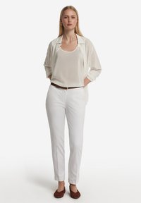 Vita byxor med slim fit, i kombination med en ljus transparent skjorta med knappar och en beige linne. Bruna slip-on skor och ett brunt bälte.