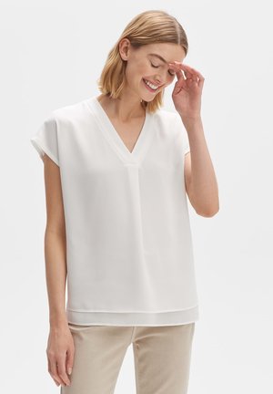 Blouse blanche à manches courtes avec un décolleté en V, en tissu lisse. Présente une coupe droite et un subtil détail de couture le long de l'ourlet.