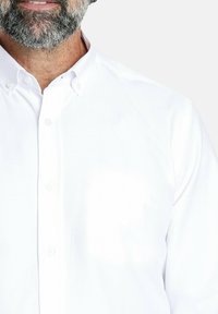 Camisa blanca de botón hecha de tela suave, con un collar clásico y detalles de botones. Diseño simple sin patrones.