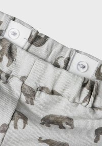 Lys grått stoff med en strukturert finish som har et mønster av brune bjørnesilhuetter. Fullført med to hvite trykknapper.