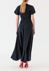 Námořnická modrá šaty s krátkým rukávem, přiléhavým korzetem, rozšířenou sukní a hladkou texturou. Spárované s červenými lodičkami na vysokém podpatku.