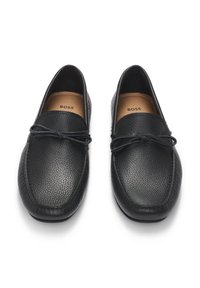 Sorte skinnloafers med teksturert finish. Designet har en rund tå og en tynn snøredetalj på overdelen. Innvendig er de foret med et lett materiale.