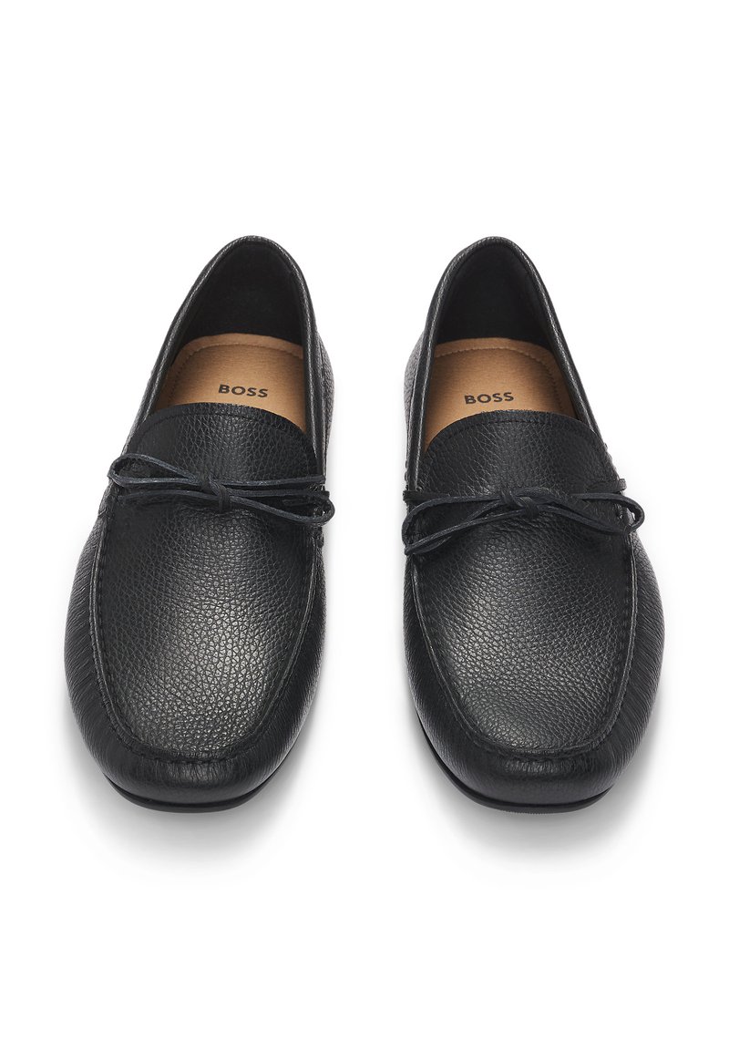 Mocassini in pelle nera con una finitura testurizzata. Il design presenta una punta arrotondata e un sottile dettaglio in pizzo sulla parte superiore. L'interno è foderato con un materiale leggero.