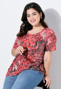 Camiseta de manga corta con un patrón rojo y negro, hecha de tela ligera, combinada con jeans azules y gafas de sol naranjas. Textura suave.