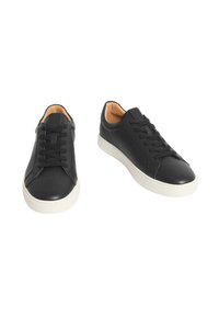 Para czarnych skórzanych sneakersów ze sznurowaniem, z białymi gumowymi podeszwami i brązowym wykończeniem wewnętrznym, pokazana z przodu oraz z kątem bocznym.