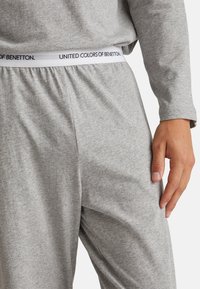 Los pantalones de lounge de algodón gris presentan una cinturilla elástica con la marca "United Colors of Benetton". Tienen una textura suave, un ajuste relajado y bolsillos en las costuras laterales.
