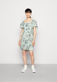 Vestido com padrão floral em verde claro, com mangas curtas e soltas, cintura ajustada e comprimento até o joelho, combinado com ténis brancos de cano alto.
