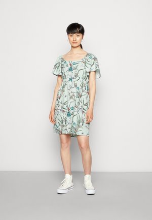 Vestido com padrão floral em verde claro, com mangas curtas e soltas, cintura ajustada e comprimento até o joelho, combinado com ténis brancos de cano alto.