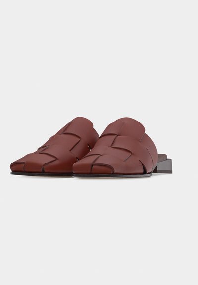 Καφέ δερμάτινα υφαντά σανδάλια τύπου slip-on με τετράγωνα δάχτυλα και χαμηλά τακούνια block πάνω σε λευκό φόντο.