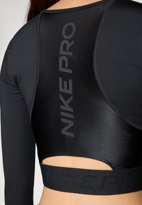 Tricou sport cu mânecă lungă de culoare neagră, având un logo texturat Nike Pro pe spate, cu un design ajustat și un finisaj din țesătură netedă.