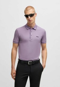 Light purple polo shirt with a slim fit, black embroidered logo, and a contrast collar. Worn with black trousers and a belt featuring a shiny buckle.