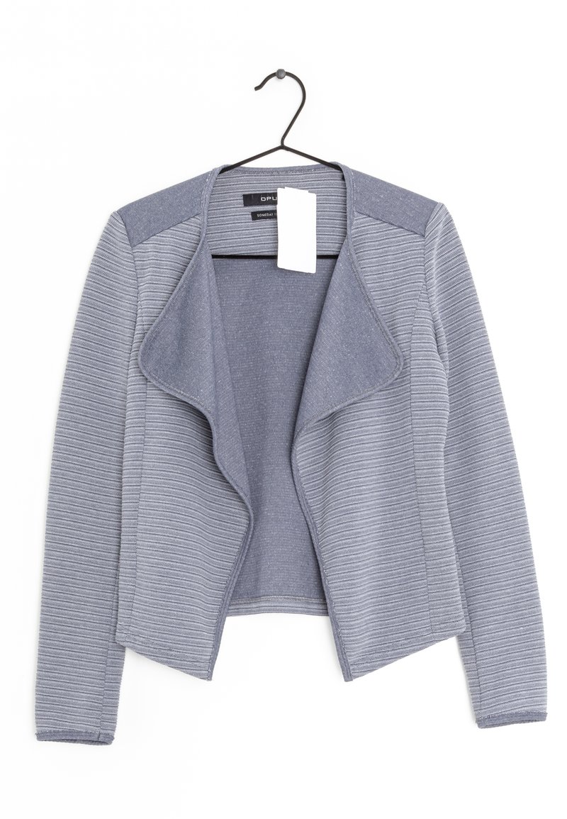 Grå stickad jacka med draperad fram, ribbad textur och fasta axelaccenter. Hänger på en svart krok med en prislapp fäst.