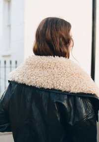 Giacca di pelle nera con un colletto di shearling beige e fluffy. Il design presenta una texture liscia e una vestibilità comoda.