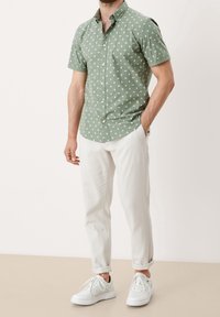 Krótki rękaw, zielona koszula w biały diamentowy wzór, zapięcie na guziki. W połączeniu z białymi chinosami podwiniętymi i białymi trampkami.