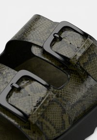 Πράσινα σανδαλάκια από δέρμα φιδιού με δύο ρυθμιζόμενες μαύρες αγκράφες, με υφή και μαύρη σόλα.