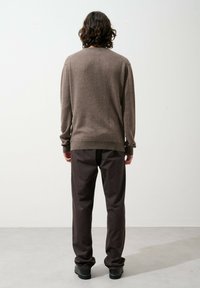 Brauner Wollpullover mit rundem Halsausschnitt und langen Ärmeln; kombiniert mit dunkelgrauen Hosen. Glatte Oberfläche, minimalistisches Design, Hosenbündchen leicht tapered.
