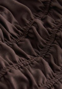 Gros plan sur un tissu marron foncé avec des coutures froncées créant des sections texturées et plissées.