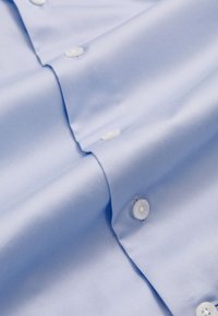 Light blue cotton dress shirt fabric folded, featuring white buttons and neat stitching along the placket and cuffs.