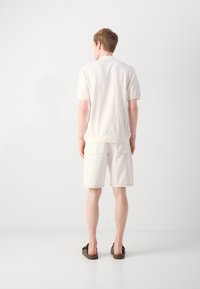 Polo en tricot crème associé à un short crème, avec une coupe décontractée et des manches courtes, porté avec des sandales de bain sombres.