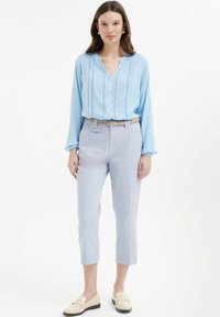 Jasnoniebieska bluzka z długim rękawem z listwą, zestawiona z jasnoniebieskimi spodniami typu cropped oraz beżowymi loafersami, z plecionym paskiem.