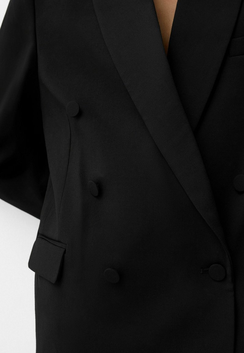 Blazer noir croisé en tissu lisse, avec de grands boutons ronds, des revers crantés et une poche poitrine.