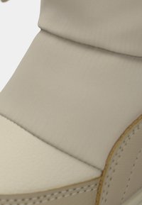 Beige laars met een gladde, textuurachtige bovenkant en een contrasterend crème ondergedeelte. Gestikte accenten benadrukken de naden.