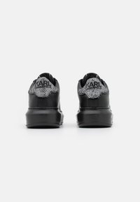 Baskets noires en cuir avec un accent en maille texturée argent et noir au niveau du talon, dotées d'une semelle épaisse et d'un logo à l'arrière.