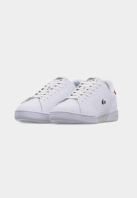 Hvite Lacoste lave sneakers med snøring, med Lacoste-logo på siden og tungen, og rød hæl-detalj.