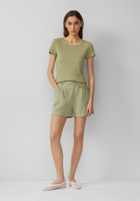 Olijfgroene geribbelde gebreide top met korte mouwen, gecombineerd met bijpassende op maat gemaakte shorts. Model draagt witte mesh platte schoenen. Eenvoudig, strak ontwerp.