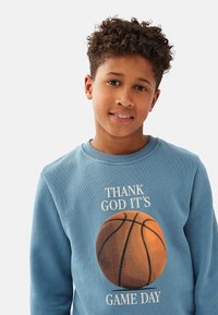 Blå sweatshirt i bomull med en basketgrafik och texten "TACK GUD FÖR ATT DET ÄR MATCHDAG." Standard design med rundad halsringning.