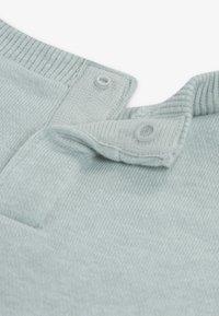 Ελαφρώς γαλάζιο πλεκτό ύφασμα με υφή. Διαθέτει κούμπωμα με κουμπί στο γιακά και λείο, ριγωτό τελείωμα.