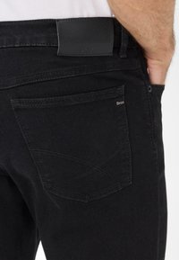 Jeans neri in denim con un'etichetta nera testurizzata sulla vita, cuciture curve sulle tasche posteriori e un design slim fit.