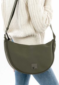 Borsa a tracolla verde oliva con spalla curva, realizzata in materiale liscio, con una targhetta logo grigia sul davanti e una tracolla regolabile.