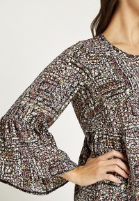 Blusa floral con base negra, pequeñas flores de colores en rosa, amarillo y blanco. Presenta mangas con volantes y un escote redondo.