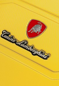 Superficie gialla testurizzata con il logo "Lamborghini" in argento e uno scudo rosso con un emblema di toro. Design chiaro con dettagli di branding ben evidenti.