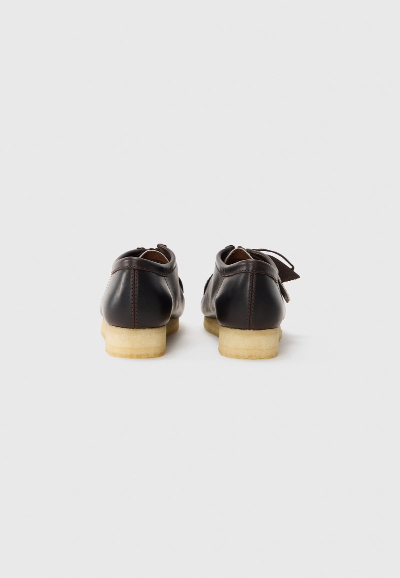 Chaussures en cuir marron avec une forme arrondie et des semelles en caoutchouc légères. Présentent un système de laçage et des détails de couture minimalistes sur la tige.