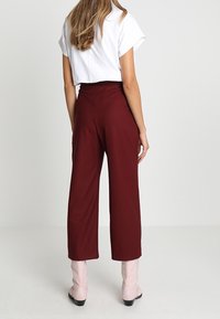 Pantalons larges bordeaux à taille haute, accompagnés d'un haut blanc à manches courtes et de bottines roses pastel. Texture de tissu lisse.