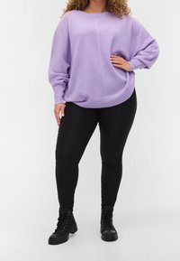 Lavenderfarbener strukturierter Pullover mit lockerer Passform, langen Ärmeln und geripptem Saum, kombiniert mit schwarzen Leggings und schwarzen Schnürstiefeln.