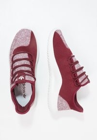 Bordeauxfärgade sportskor med en andningsbar stickad ovandel, texturerade detaljer, vit gummisula och elastiska snören för en säker passform.