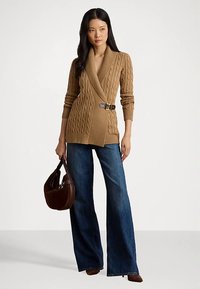 Ruda megzta kardiganas su užrišamu dizainu ir diržo sagtimi, derinamas su mėlynais plačiomis kojų džinsais ir ruda peties rankine.