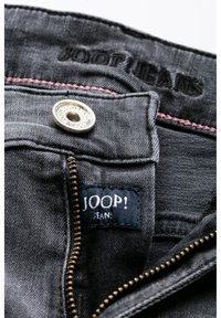 Tmavě šedé džínové kalhoty s pozlaceným zipem, kontrastním růžovým prošitím a černou štítkem s nápisem "JOOP! JEANS." Vytlačené logo v horní části.