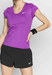 Top atlético morado de manga corta con un diseño de escote en V y pantalones cortos deportivos negros. Logo de Nike en ambas prendas; la tela parece suave y ligera.