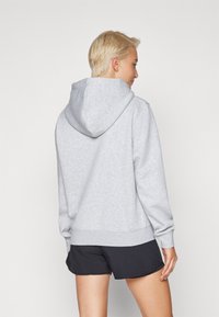 Felpa grigia con cappuccio realizzata in tessuto morbido, caratterizzata da una vestibilità rilassata, polsini e orlo a costine. Indossata con pantaloni sportivi neri, design minimale.