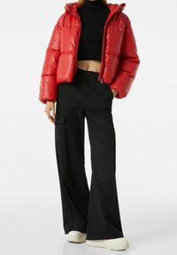 Červená péřová bunda s předním zipem a kapucí, spárovaná s černými širokými cargo kalhotami s bočními kapsami a hladkou texturou.