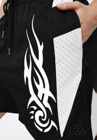 Calções atléticos pretos com textura de rede, apresentando padrões tribais brancos de um lado e um painel branco, com cintura elástica e cordão.