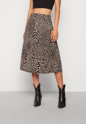 Kvinde iført højtaljet midi-nederdel med beige og sort abstrakt dyreprint, sort crop top og sorte ankelstøvler med spids tå.